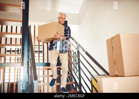 Moving days running like a well oiled machine. a handsome mature man carrying a box on moving day. Stock Photo