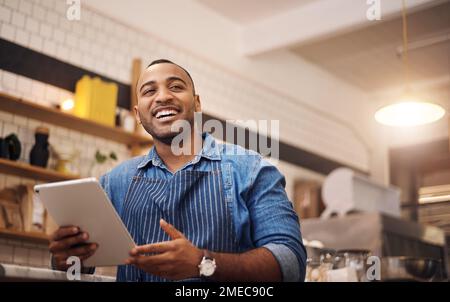 Stay positive, work hard and make it happen. a handsome young businessman standing alone in his cafe and using his tablet. Stock Photo