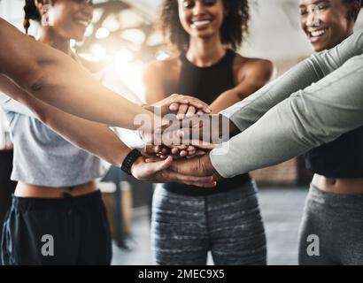Getting a healthy dose of motivation. a group of young people joining their hands together in solidarity at a gym. Stock Photo