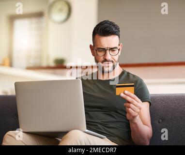Just a small splurge...a handsome young man using a laptop and credit card at home. Stock Photo