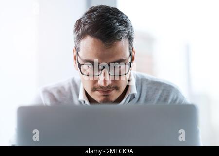 Focused on finishing up on his latest project. a young businessman working on a laptop in an office. Stock Photo