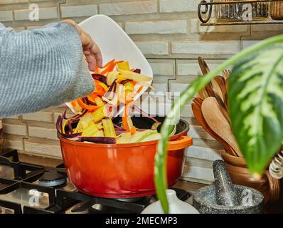 Chef tosses pieces of three-colored carrots into cooking pot in the kitchen Stock Photo