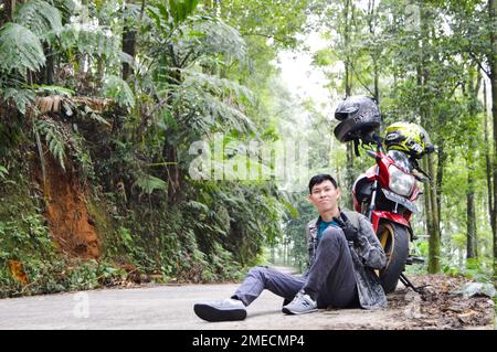 posing in front of a motorbike with a beautiful and cool view of the pine forest, With Selected Focus. Stock Photo