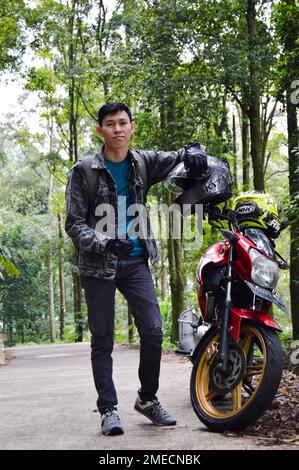 posing in front of a motorbike with a beautiful and cool view of the pine forest, With Selected Focus. Stock Photo