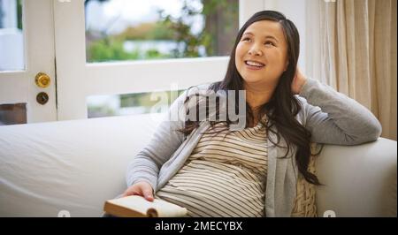 Reading is great for helping first time expectant moms. a pregnant woman looking thoughtful while reading a book at home. Stock Photo