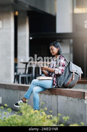 Texting her friends during recess. Full length shot of an attractive young female student using her cellphone while sitting outside on campus. Stock Photo