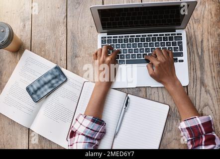 Using online resources to complete university projects. High angle shot of an unrecognizable female student using her laptop while sitting outside on Stock Photo