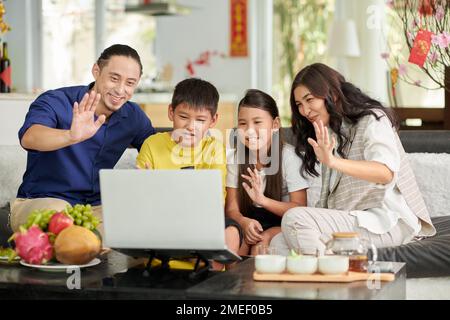Joyful parents and children waving with hands when making video call at Tet celebration Stock Photo