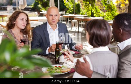Two happy couples having lunch at open-air restaurant summer Stock Photo
