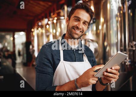Business is going great like usual. Portrait of a cheerful young barman browsing on a digital tablet while patiently waiting at the bar for customers Stock Photo