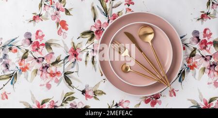 Beige round plates and golden cutlery on a white tablecloth with floral pattern, table top view, above. Flat lay design. Ceramic utensils, serving. Ta Stock Photo