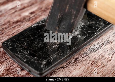 Broken smartphone with shattered cracked glass touchscreen display and hammer closeup Stock Photo