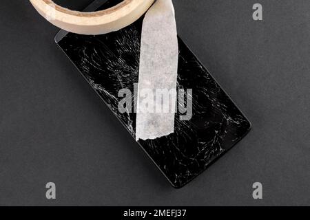 Broken black mobile phone with shattered glass screen covered with adhesive repair tape. Conceptual view Stock Photo