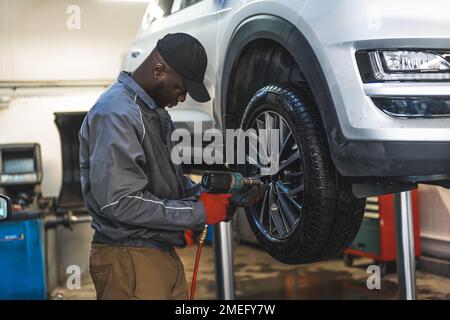A mechanic working on a lifted-up car - Changing wheels using an electric wrench. High-quality photo Stock Photo