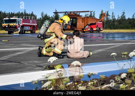 A firefighter assigned to Navy Region Northwest Fire and Emergency Services attends to an injured airman during an aircraft mishap drill on the Naval Outlying Field in Coupeville, Washington August 17, 2022. The joint training tested the aircraft mishap response procedures of our Federal Fire, Search and Rescue, and local first responders. Stock Photo