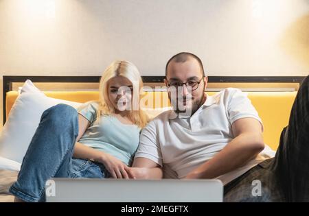 Young couple lying on couch at home looking at laptop. Stock Photo