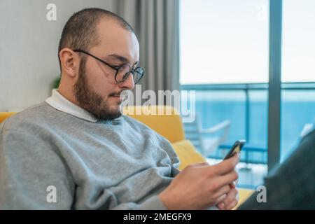 Man using smartphone at home, browsing internet news, social media or downloading application or app. Stock Photo