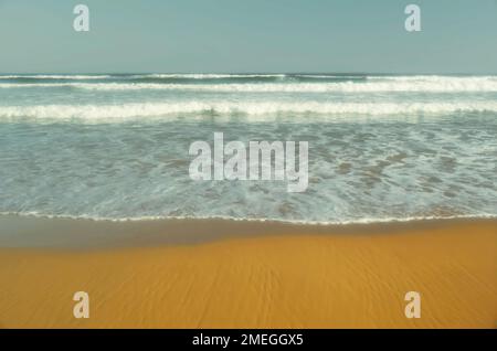 Incoming whitewater waves rolling onto a sandy beach Stock Photo