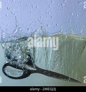 scissors fall into the water. sprays, drops and bubbles Stock Photo