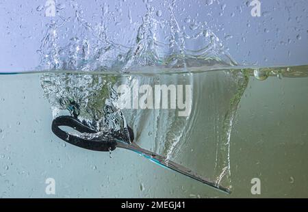 scissors fall into the water. sprays, drops and bubbles Stock Photo