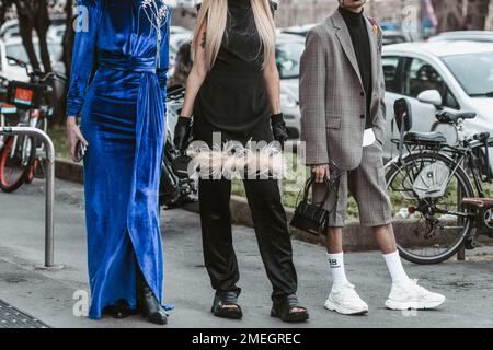 Milan, Italy - February 24, 2022: Woman in long blue dress near female in black outfit with feathers and man in checkered suit with shorts and handbag Stock Photo