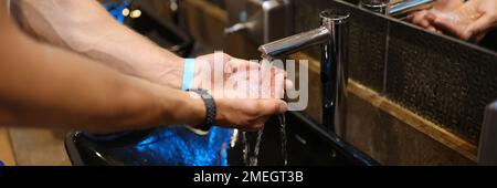 Man washes hands in the sink in bathroom at home checking temperature by touching running water with hand Stock Photo