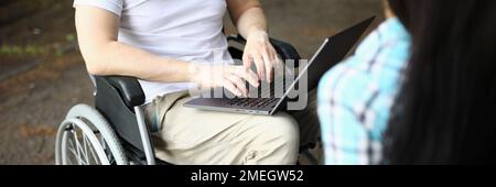 Man in wheelchair and woman work remotely while sitting in park Stock Photo