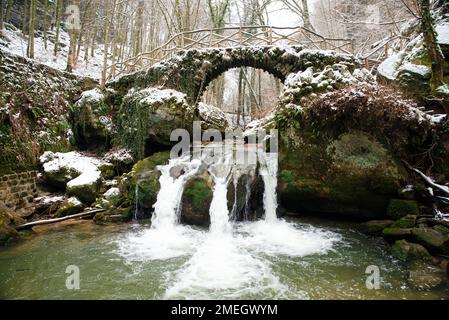 Scheissendempel waterfall, river Black Ernz with stone bridge covered with snow, Mullerthal trail in Waldbillig, Luxembourg in winter Stock Photo