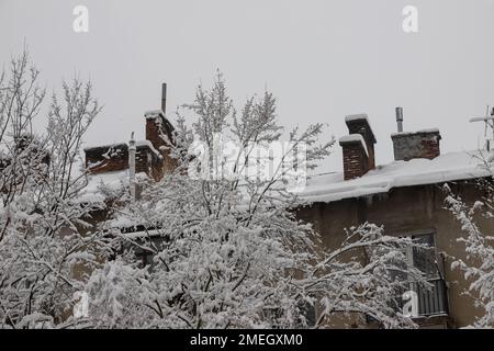 Facade of a residential building in the suburbs during a snowfall. The wall of the house and the balcony are covered with snow. Tree branches covered Stock Photo