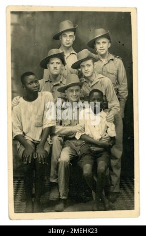 Original and clear WW2 portrait postcard of happy group of soldiers, possibly Australians allies wearing desert slouch or bush hats, allows rifle slung over shoulder, posing for a photo with African children, dated 1943. Bert is one of the men named. Possibly North Africa, towards the end of the military campaign there (ended in May 1943), so maybe a leaving souvenir photo. Stock Photo