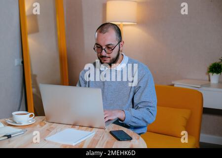 Man in eyeglasses working at laptop at home. Internet buisiness, freelance or distance job concept. Stock Photo