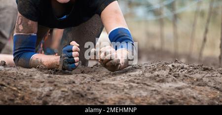 Mud race runners. Crawling,passing under a barbed wire obstacles during extreme obstacle race Stock Photo