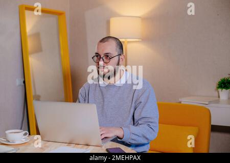 Man in eyeglasses working at laptop at home. Internet buisiness, freelance or distance job concept. Stock Photo