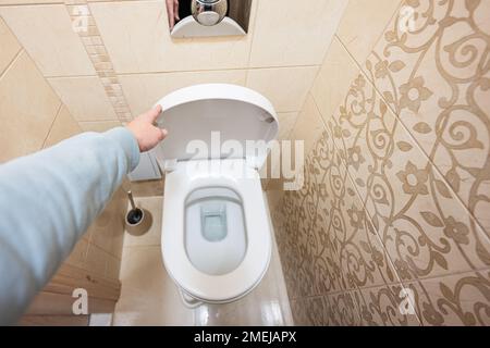 Hand of a man is closing the toilet lid. Stock Photo