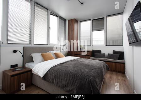 Home interior design of bedroom with bed and wooden wardrobe placed in corner near window in modern apartment Stock Photo