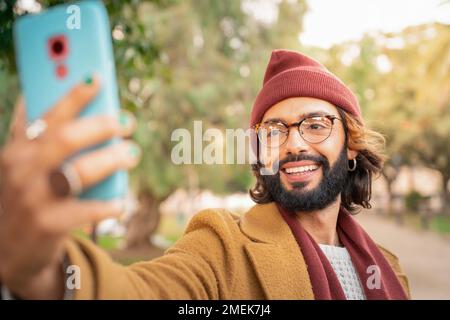 Attractive young caucasian man with glasses and beard taking a selfie outdoors in the park. Stock Photo