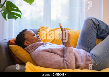 Short-haired woman lying on the sofa using social networks with her smartphone and relaxing while resting. Concept: technology, rest Stock Photo