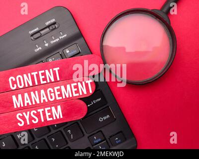 Magnifying glass with the word CONTENT MANAGEMENT SYSTEM on red background. Stock Photo