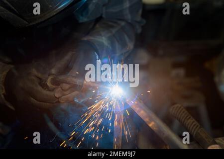 Worker welding metal with sparkles on it, using semi automatic welding machine shielded by an argon gas in order to achieve seam Stock Photo