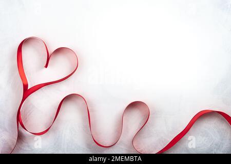 Red ribbon in shape of heart on the vintage white-grey background. Festive concept for Valentines day. Top view with copy space. Stock Photo