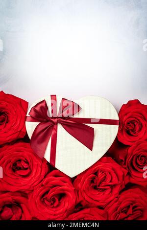Red roses and gift box in shape of heart on the vintage white-grey background. Festive concept for Valentines day. Top view with copy space. Stock Photo