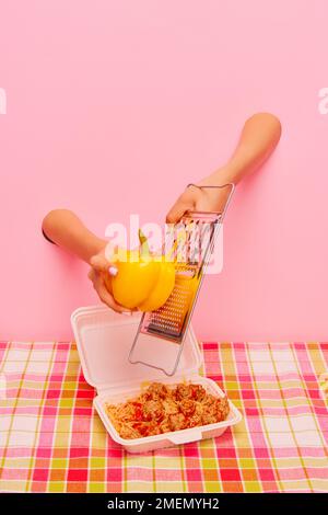Food pop art photography. Female hand sticking out pink paper and grating yellow pepper on spaghetti with meatballs Stock Photo
