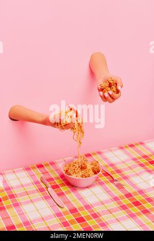 Food pop art photography. Female hand sticking out pink paper and holding spaghetti and meatballs. Dinner time Stock Photo