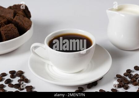Coffee with milk - a cup of coffee and a milk jug on a white background, a place for text, a delicious breakfast. Stock Photo