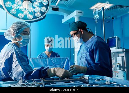 Operating room team. Focused surgeon operating on patient with assistants in hospital operating theatre indoors Stock Photo