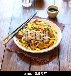 Stir-fried noodles with Chinese sausage and shiitake, served in wide bowl with chopsticks and bowl of soy sauce Stock Photo