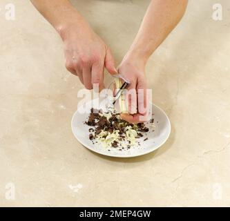 Using a peeler to produce white and dark chocolate shavings Stock Photo