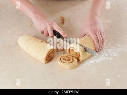 Cinnamon Rolls, cutting rolled up dough into equal pieces using serrated knife Stock Photo