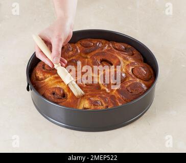 Cinnamon Rolls, brushing glaze on baked cinnamon rolls Stock Photo