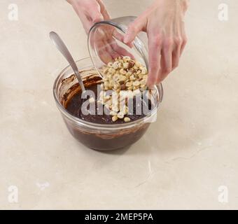 Making Chocolate and Hazelnut Brownies, tipping chopped nuts into batter Stock Photo